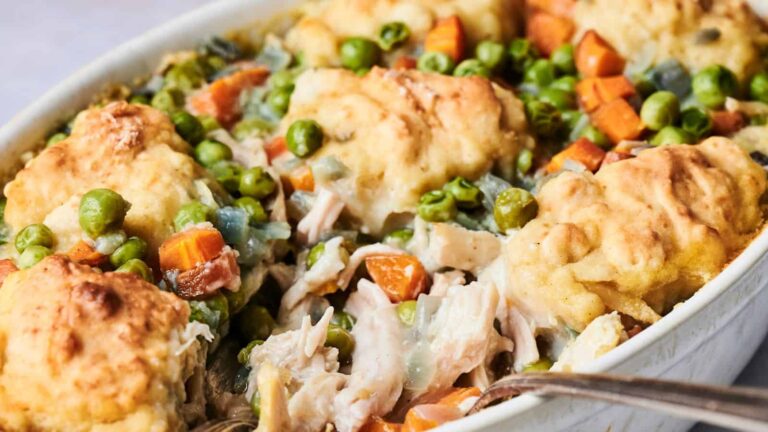 A casserole dish filled with chicken pot pie, featuring chunks of chicken, peas, carrots, and fluffy biscuit topping.