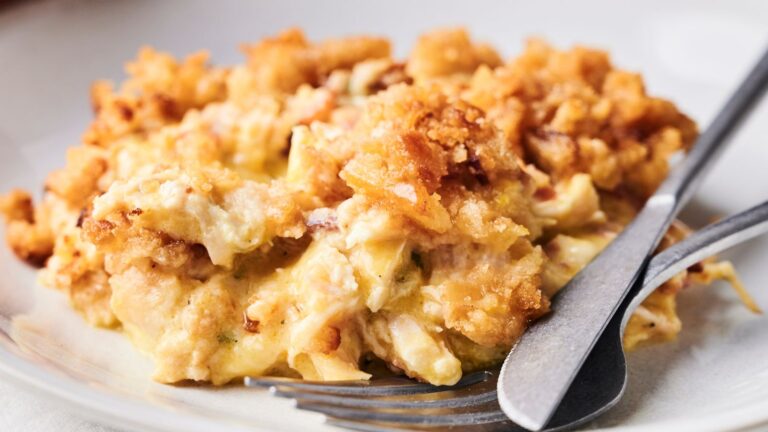 Close-up of a creamy macaroni and cheese dish with a crunchy breadcrumb topping, served on a plate with a fork and knife.