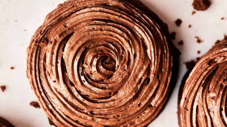Close-up of a chocolate frosting swirl on a round cookie with crumbs around it.