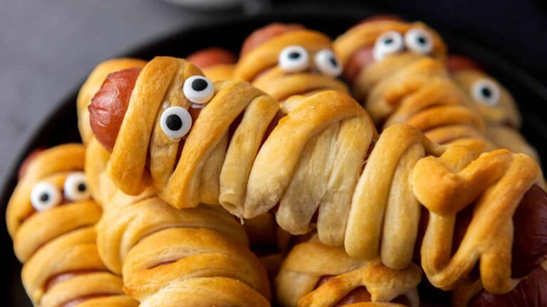 Hot dogs wrapped in dough to resemble mummies, with candy eyes, on a plate.