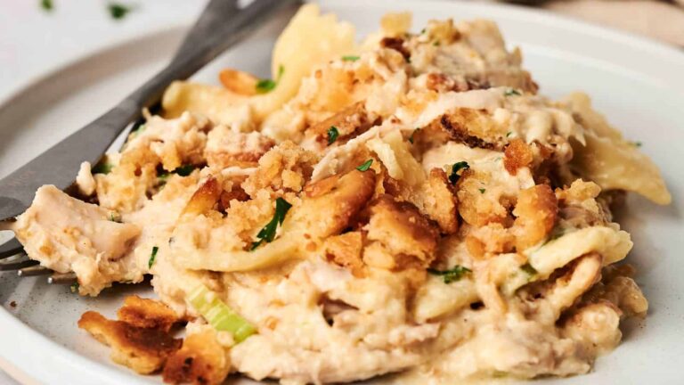 A plate of creamy chicken pasta topped with breadcrumbs and herbs, with a fork and knife on the side.