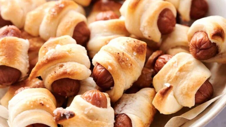 A close-up of pigs in a blanket—mini sausages wrapped in golden-brown pastry—on a plate.