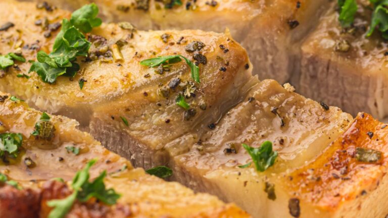 Close-up of seasoned and cooked slices of pork belly garnished with fresh herbs.