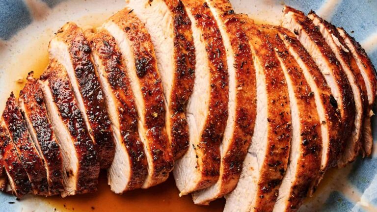 Sliced roasted turkey breast on a plate with visible seasoning and juices.