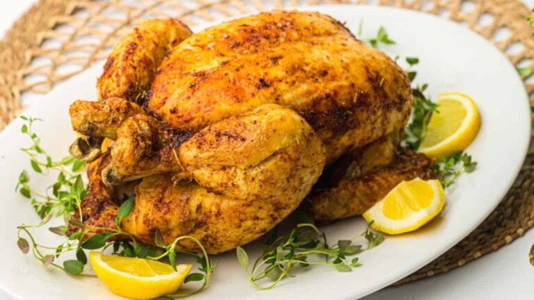 Roasted chicken with herbs and lemon wedges on a white plate.