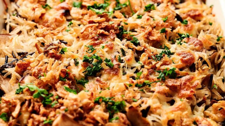 Close-up of a baked dish with shredded potatoes, crispy onions, and chopped parsley on top.