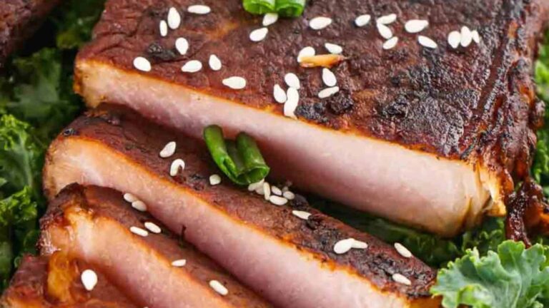 Slices of grilled meat garnished with sesame seeds and green onions on a bed of leafy greens.