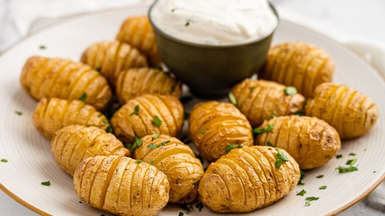 A plate of sliced baked potatoes garnished with herbs, accompanied by a bowl of white dipping sauce.