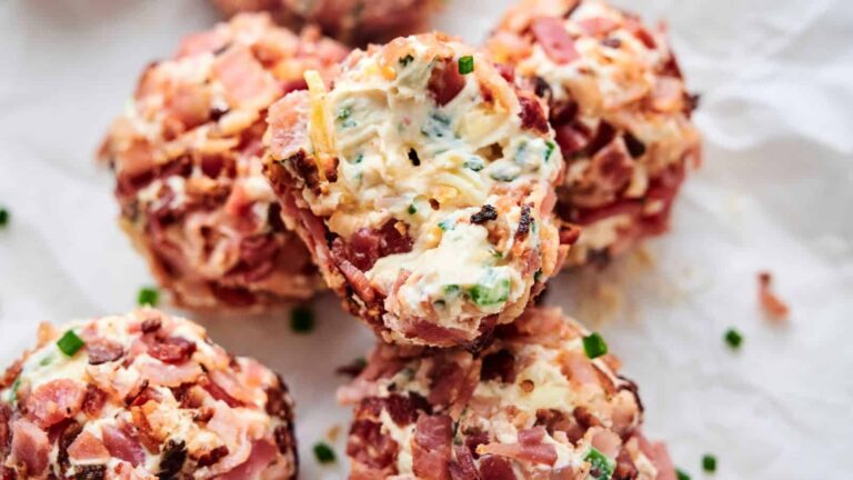 Close-up of bacon-wrapped cheese balls with chopped chives on top, placed on white parchment paper.