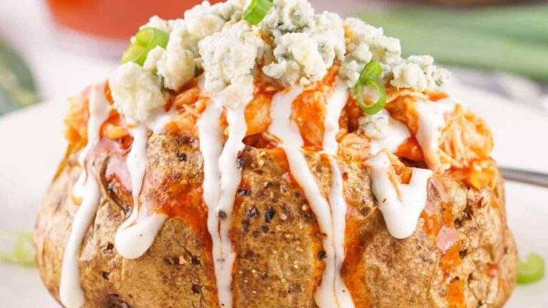 Baked potato topped with buffalo chicken, crumbled blue cheese, and green onions, drizzled with white sauce.