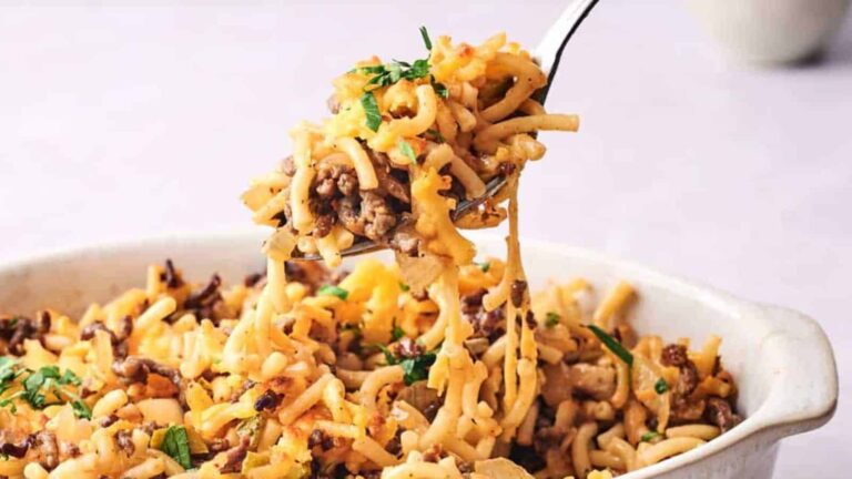 A fork lifts a portion of macaroni and beef casserole from a white baking dish, garnished with parsley.