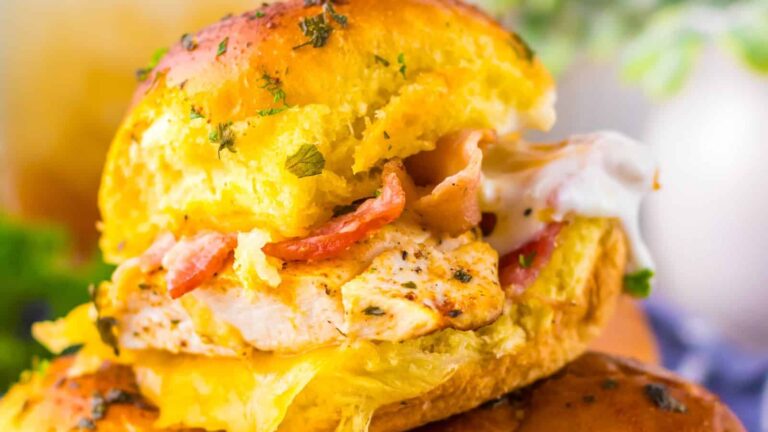 A close-up of a sandwich with grilled chicken, bacon, and melted cheese in a toasted, seasoned bun.