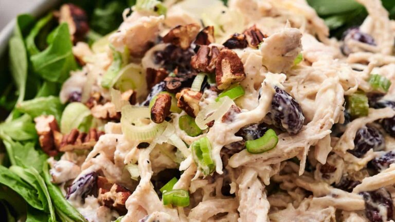 Chicken salad with shredded chicken, chopped pecans, sliced green onions, and dark grapes on a bed of fresh spinach.