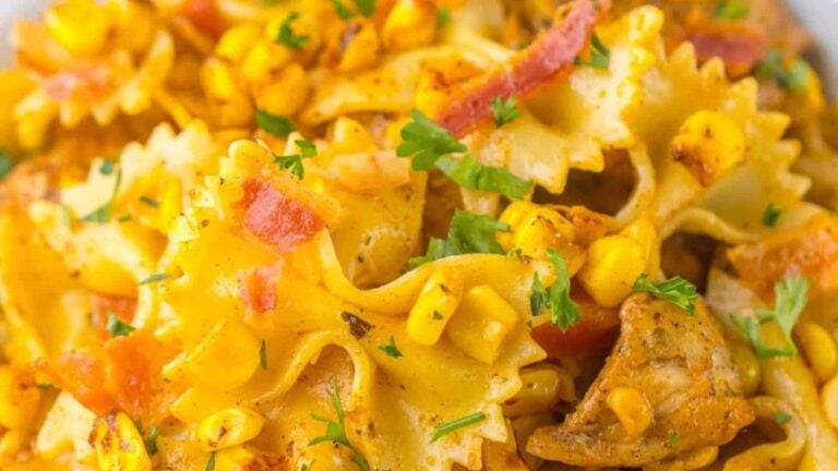 A close-up of bowtie pasta with corn, diced tomatoes, bacon, and chicken pieces, garnished with parsley.
