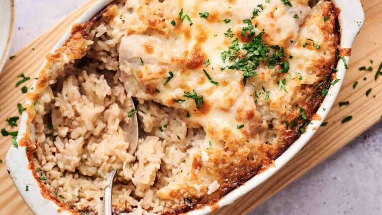 Baked creamy rice casserole topped with melted cheese and garnished with herbs in a white dish, with a spoon.