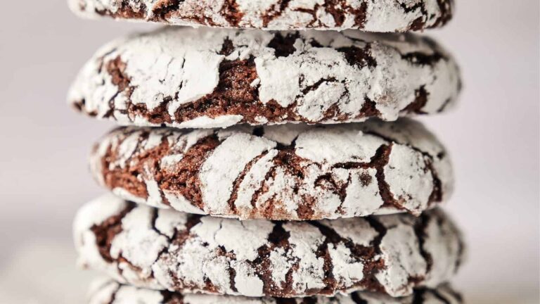 A stack of four chocolate crinkle cookies dusted with powdered sugar, showing crackled surfaces.