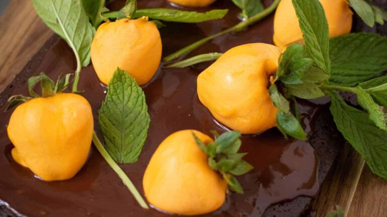 Orange fruits on a chocolate-covered surface, garnished with fresh green leaves.