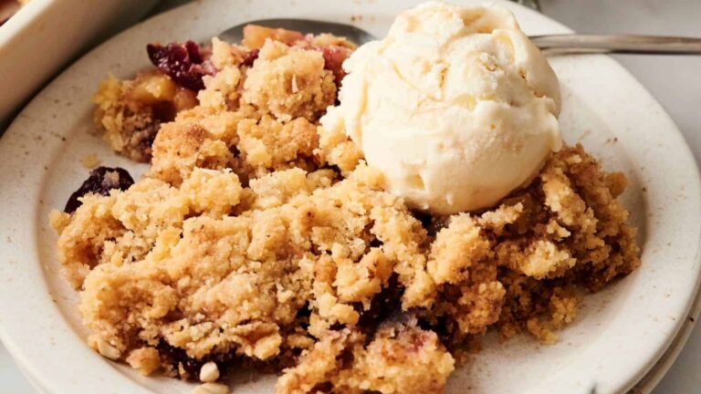 A plate of fruit crumble topped with a scoop of vanilla ice cream.