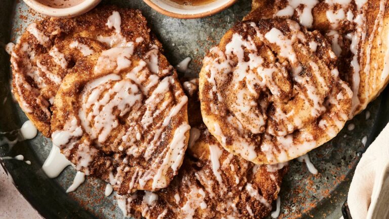 Close-up of iced cinnamon rolls with visible swirls, drizzled with glaze, on a plate.
