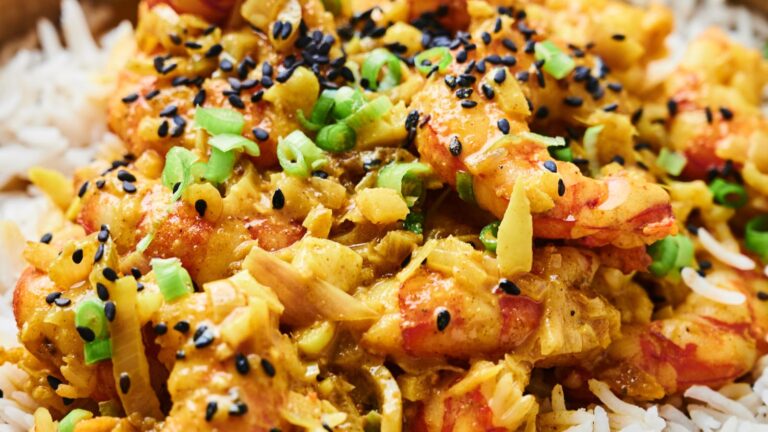 Close-up of shrimp curry on rice, garnished with green onions and black sesame seeds.