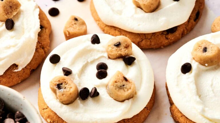 Cookies topped with white frosting, chocolate chips, and cookie dough pieces.
