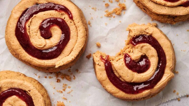 Swirled peanut butter and jelly cookies on parchment paper, with one cookie partially eaten, and crumbs scattered around.