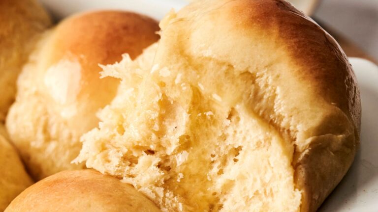 Close-up of freshly baked golden-brown dinner rolls, with one roll partially broken to reveal a soft, fluffy interior.