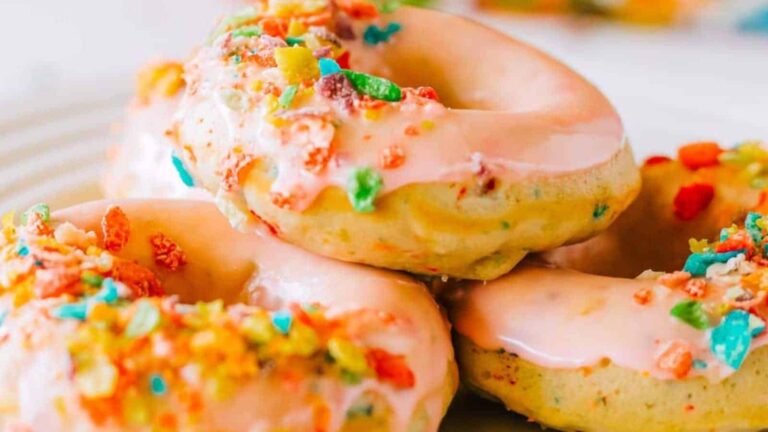 A pile of donuts with pink glaze topped with colorful cereal pieces on a white plate.