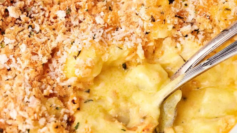 Close-up of a creamy mac and cheese dish with a golden breadcrumb topping and a spoon scooping from the center.