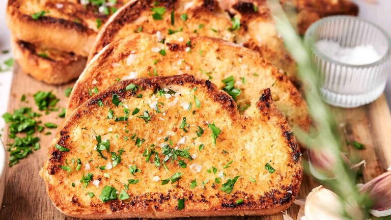 Slices of toasted garlic bread garnished with chopped parsley, arranged on a wooden board with a small bowl of salt nearby.