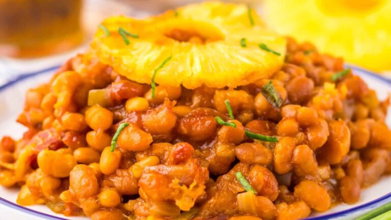 A plate of baked beans garnished with a ring of pineapple and chopped herbs.