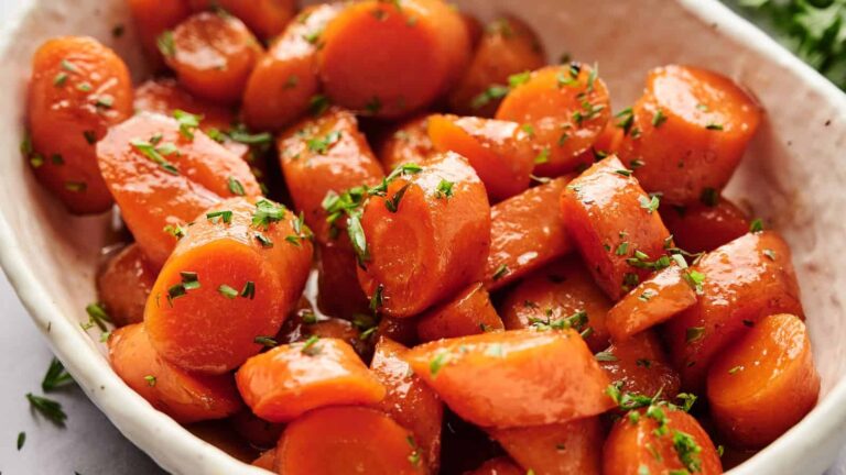 A white bowl filled with glazed carrot slices, garnished with chopped herbs.