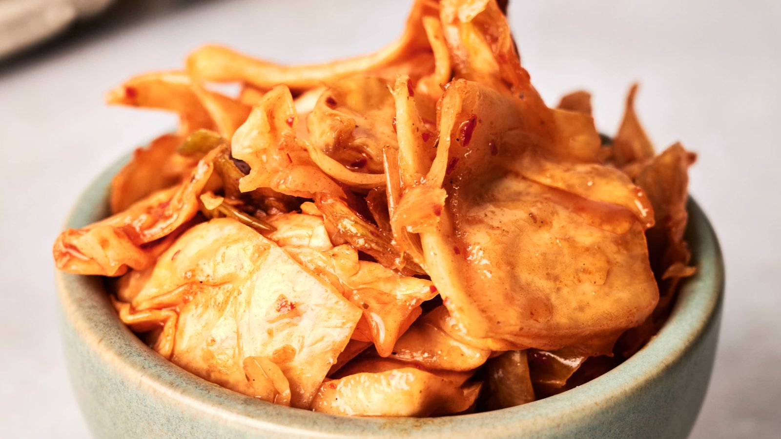 A bowl of spicy, pickled kimchi cabbage on a light-colored surface.