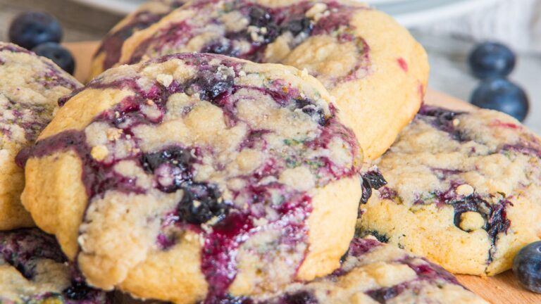 Close-up of blueberry cookies with visible fruit and crumble topping on a wooden surface.