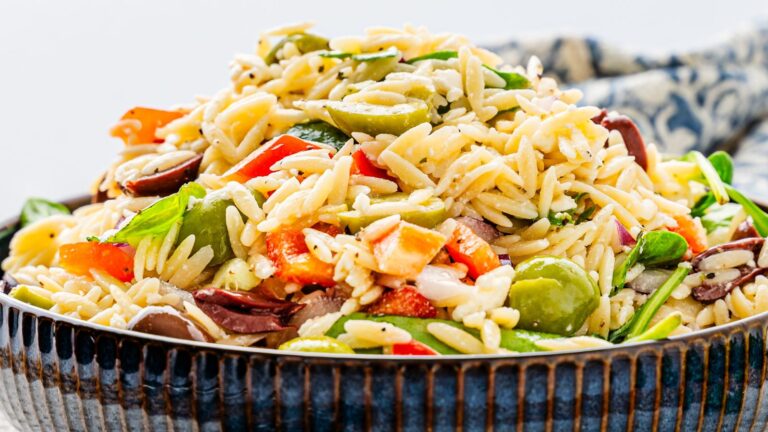 A bowl of orzo pasta salad with bell peppers, olives, spinach, and herbs.
