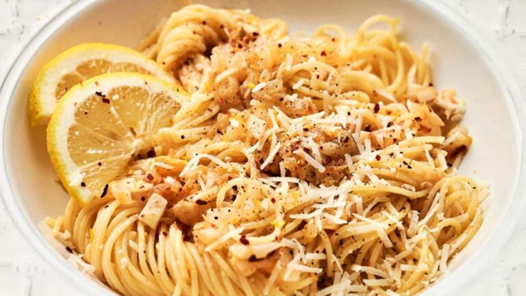 A bowl of spaghetti topped with grated cheese, red pepper flakes, and lemon slices.