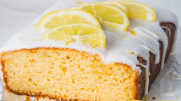 A sliced lemon cake topped with white icing and lemon slices.