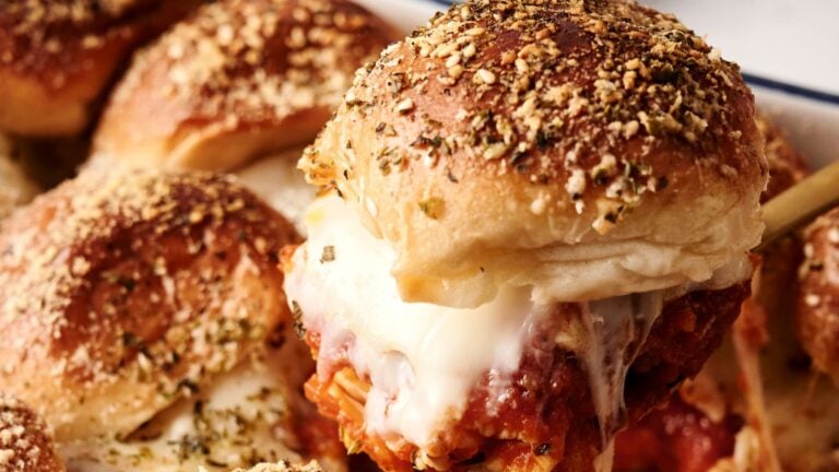 Close-up of baked meatball sliders with melted cheese and seasoned buns.
