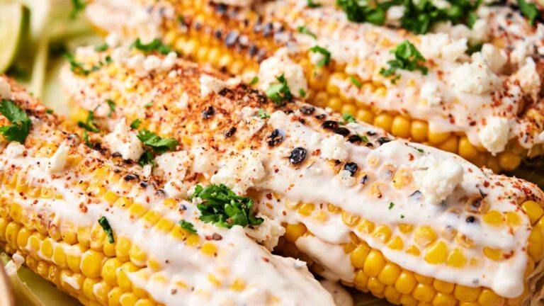 Grilled corn on the cob topped with creamy sauce, cheese, chili powder, and garnished with fresh parsley.