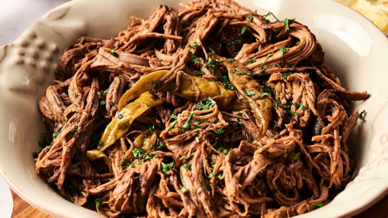 A bowl of shredded beef garnished with green chili peppers and chopped herbs.