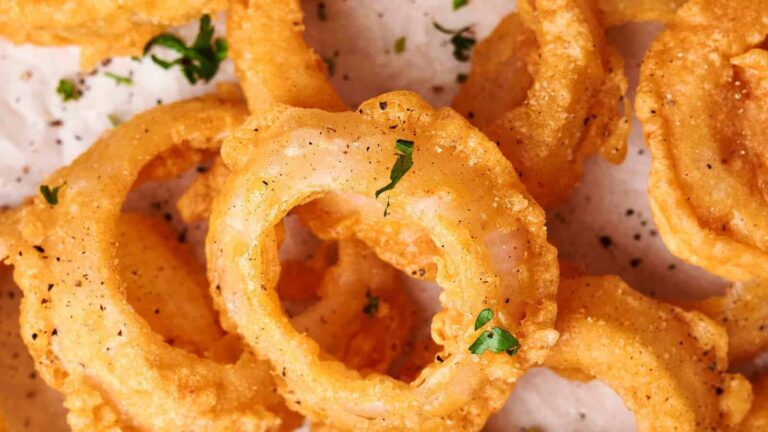 Close-up of crispy golden onion rings sprinkled with black pepper and garnished with small green herbs.