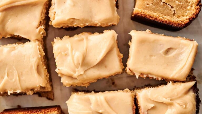 Close-up of frosted blondie squares arranged on a surface, showing a smooth, creamy topping on a light golden base.