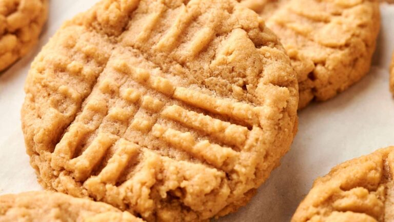 Close-up of peanut butter cookies with a crisscross pattern on top, resting on a baking sheet.