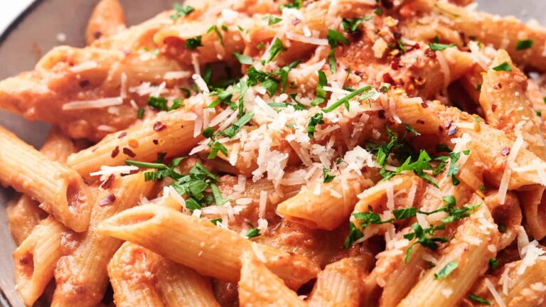 Close-up of a plate of penne pasta coated in a creamy tomato sauce topped with grated cheese and chopped parsley.