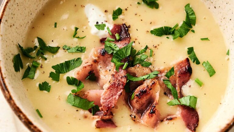 A bowl of creamy soup topped with crispy bacon bits and chopped parsley.