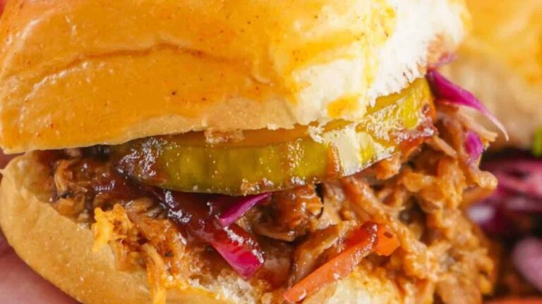 A close-up of a barbecue pulled pork sandwich with pickles and cabbage in a bun.