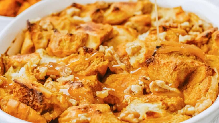 Close-up of bread pudding topped with caramel sauce and chopped walnuts in a white dish.