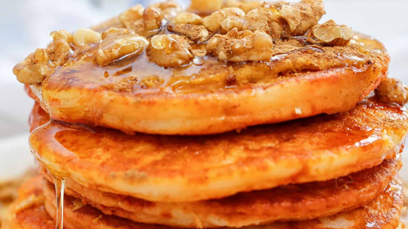 A stack of pumpkin pancakes topped with walnuts and drizzled with syrup.
