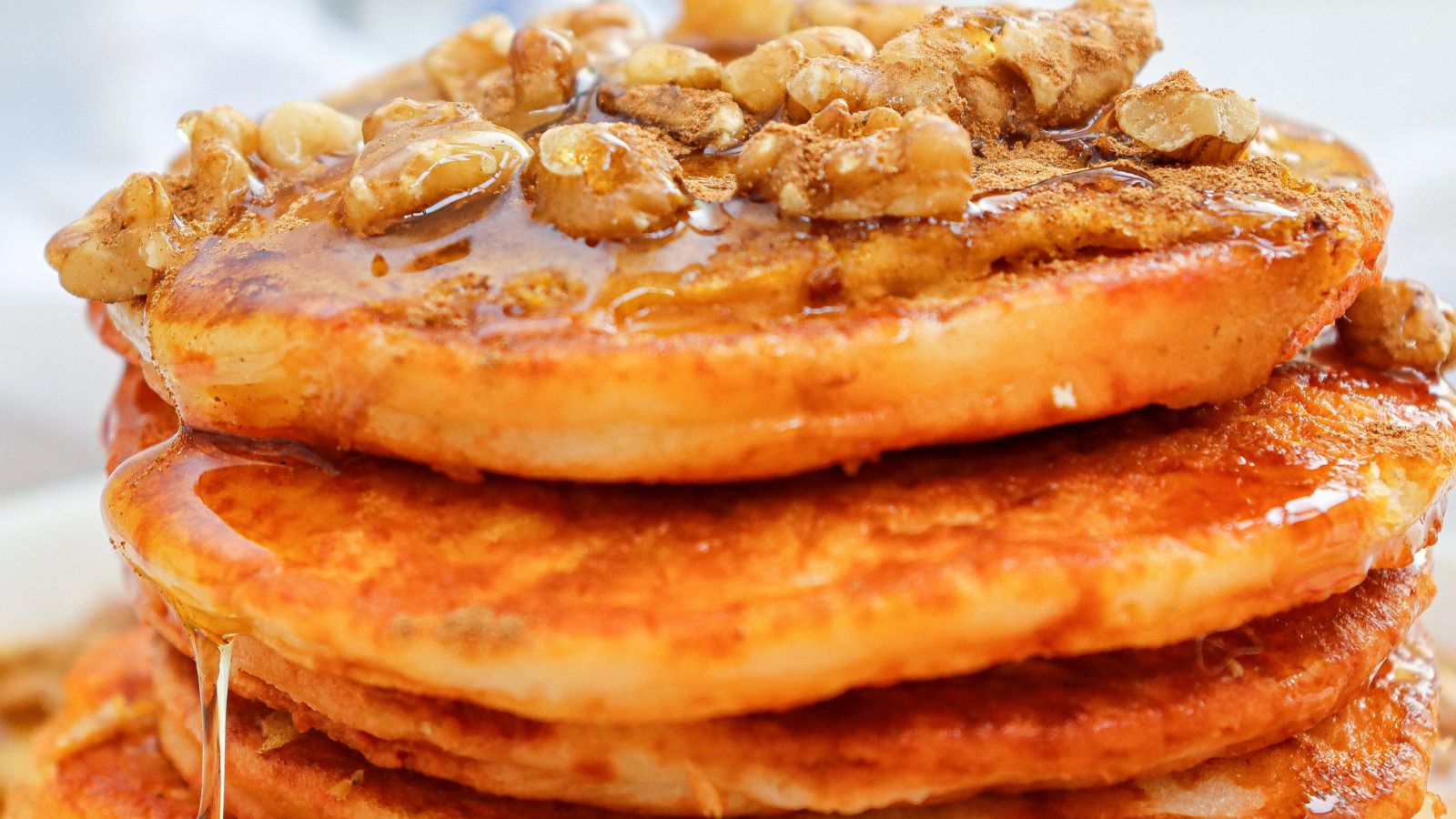 Close-up of a stack of pancakes topped with walnuts and drizzled with syrup.