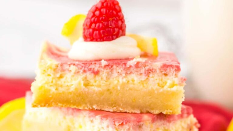 A close-up of two stacked dessert bars with a pink and yellow swirl, topped with whipped cream, a raspberry, and lemon zest.